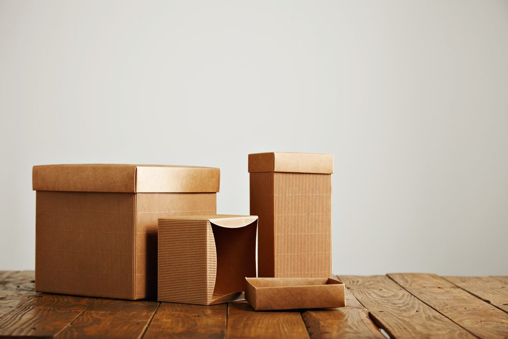 Mockups of blank brown corrugated cardboard boxes Unlabeled similar boxes of different shapes and sizes on an uneven wooden table isolated on white